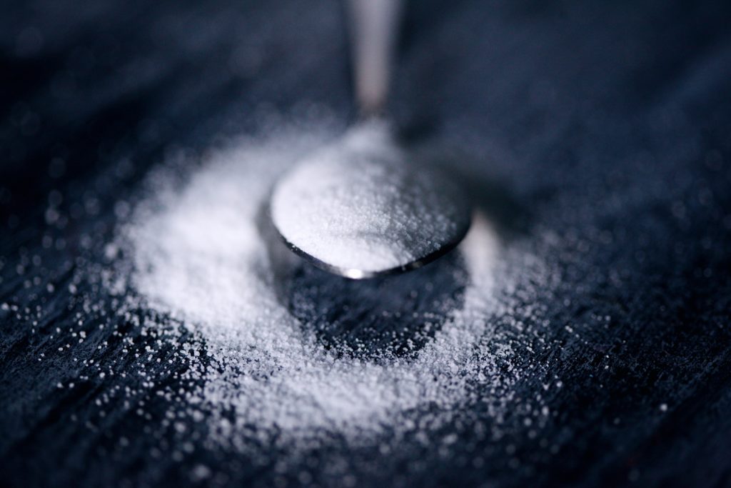 A spoonful of white sugar on a black tabletop.